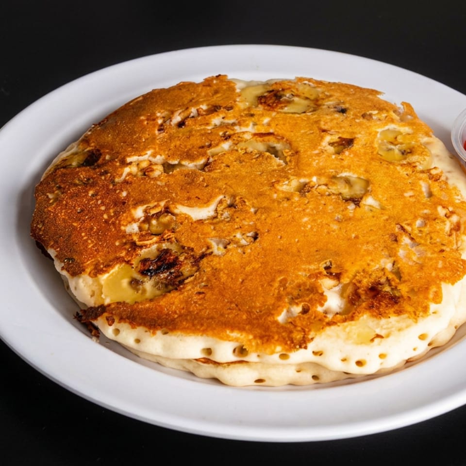 Golden griddled stuffed pancake on a white plate, accompanied by a cup of amber dipping sauce and wrapped napkin.
