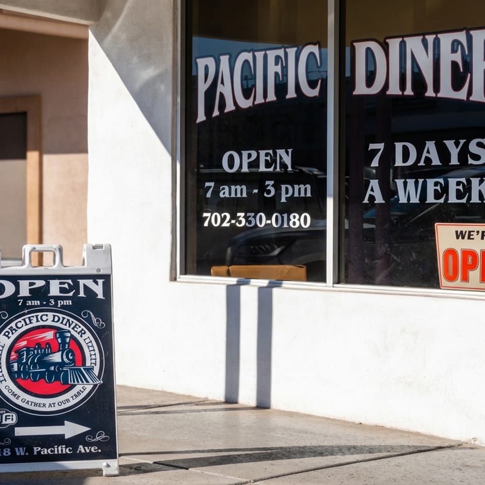 Pacific Diner storefront with open signs, operating hours, phone number, and sidewalk sandwich board pointing toward the entrance.