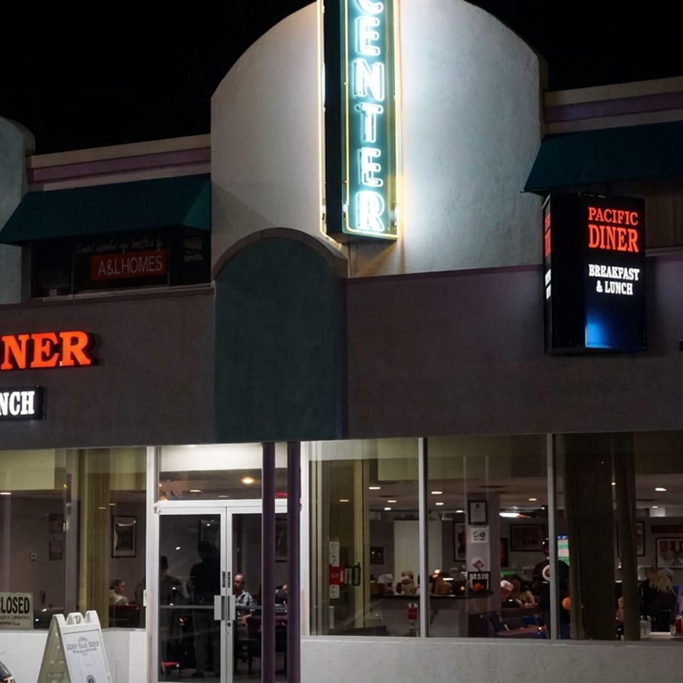 Pacific Diner storefront at night, illuminated with neon signage reading “Breakfast & Lunch,” with diners visible through the windows.